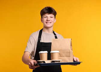Teenage boy with order working as waiter on orange background