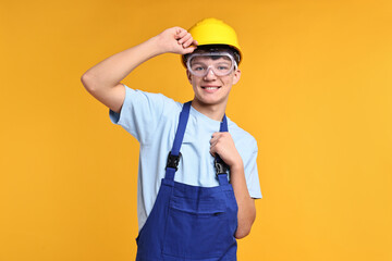 Teenage boy in hardhat and protective mask working as builder on orange background