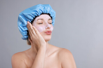 Woman with shower cap and cream on her face against grey background