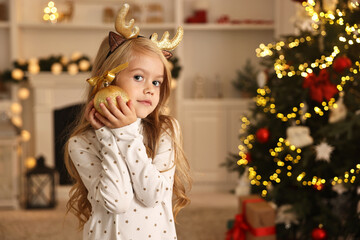 Little girl with Christmas ornament at home, space for text