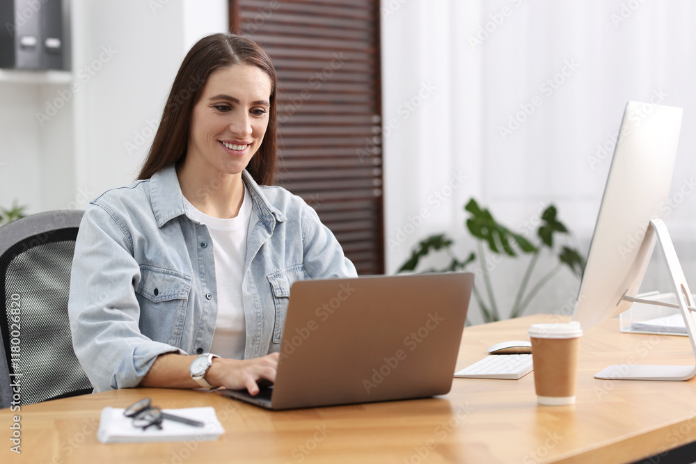 Poster programmer working on laptop and computer at wooden desk indoors