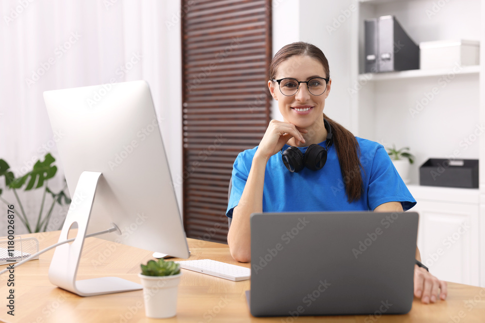 Poster programmer working on laptop and computer at wooden desk indoors