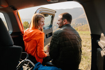 Couple Enjoying Scenic Mountain View From Car Trunk Outdoors