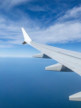 Airplane wing flying over blue ocean under cloudy sky