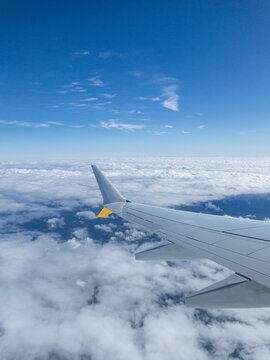 Airplane wing flying above the clouds in blue sky