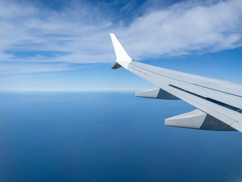 Airplane wing flying over blue ocean on sunny day