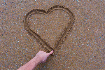 Person drawing a heart in the sand with their finger