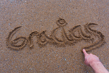 Handwriting 'Gracias' in the sand with a hand finishing the word