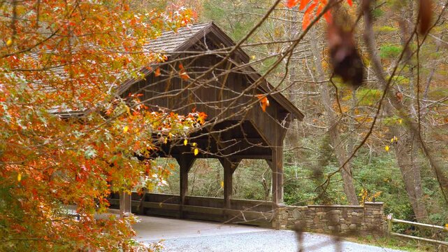 The entrance to a covered bridge framed with the red leaves of a tree adorned in its autumn foliage.
