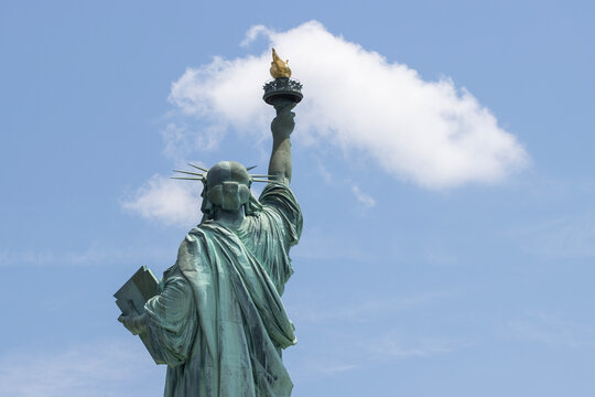 Rear view of the Statue of Liberty on the Liberty Island in New York against a blue sky and clouds.