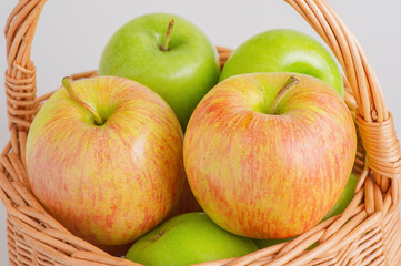 Two different varieties of apples in a wicker basket on a gray background. Fruits, apples.