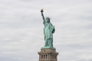 The Statue of Liberty standing on a pedestal on the Liberty Island in New York against a cloudy sky.