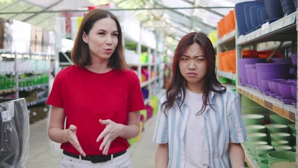 Two multiracial lesbians in a garden store are looking for a pot for their houseplants, enjoying the shopping experience together.