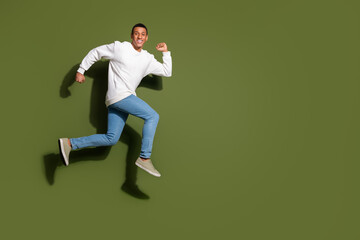 Young man in casual fashion jumping joyfully against a khaki background, expressing happiness and...