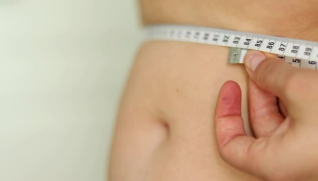 Close up of a female measuring the belly with a tape. Overweight chubby belly type.