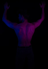 Junger Mann aus Indien steht mit freiem Oberk&ouml;rper in buntem Licht und posiert