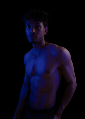 Fototapeta premium Junger Mann aus Indien steht mit freiem Oberkörper in buntem Licht und posiert