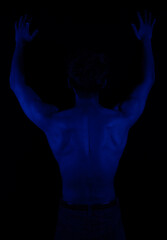 Junger Mann aus Indien steht mit freiem Oberk&ouml;rper in buntem Licht und posiert