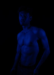 Junger Mann aus Indien steht mit freiem Oberk&ouml;rper in buntem Licht und posiert