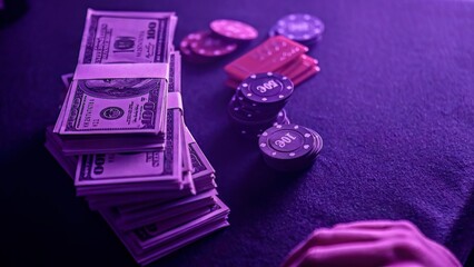 Casino chips and stacks of hundred dollar bills resting on purple felt table