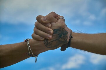 Two people holding hands showing support and friendship against blue sky