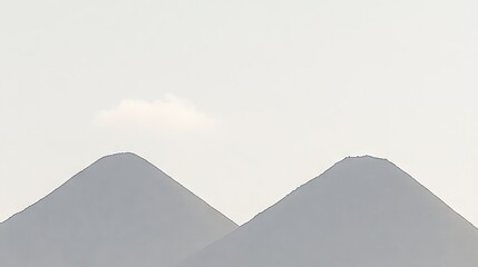 Misty volcanic peaks silhouetted against pale sky. Possible use for wallpaper or nature photography.
