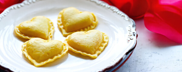Heart-shaped ravioli arranged on a decorative plate with pink fabric accents for a special occasion. Valentine’s Day idea, date, engagement party, love party, eat, food