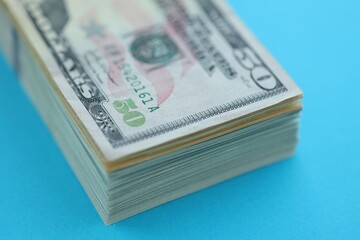 Big amount of fifty dollar bills in thick stack lies on bright blue color paper background
