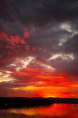 Experience the stunning beauty of a sunset over calm waters adorned by a dramatic cloudscape