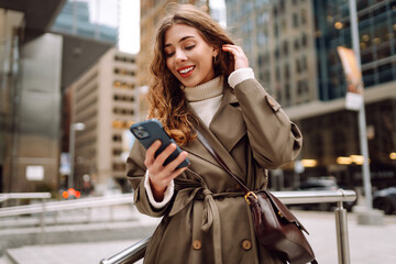 Fototapeta premium Portrait of happy woman with smartphone in the street city. Concept of vacation, blogging, technology, weekend.