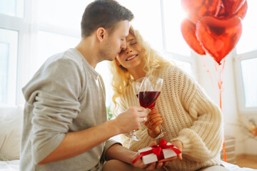 Happy couple drinking red wine at home. Romantic day together. Leisure, celebration and Valentine’s Day concept.