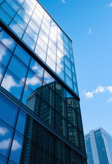 Modern office building with glass facade reflecting blue sky and clouds. Architecture, business center, corporate headquarters, cityscape