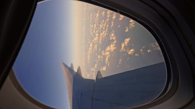view from the airplane window to the wing and clouds at sunrise, blue sky