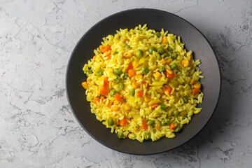 Top view of a bowl with fried rice with vegetables, onion, bell pepper, carrot, green peas. Vegetarian food served