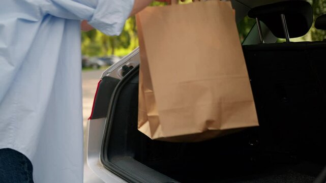 Unknown Caucasian grandmother aged shopper woman mature buyer automobile owner customer client female hands opening car trunk vehicle boot loading shopping bags purchases groceries outside parking