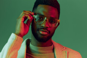 Portrait of a confident young Black man with glasses, showcasing a stylish outfit against a vibrant green and red background, perfect for fashion and lifestyle concepts