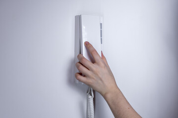 Hand holding a white intercom handset mounted on a wall, minimalist interior design concept