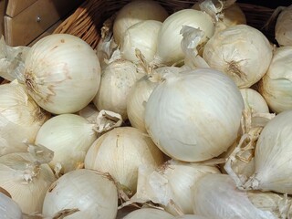 White and regular onions are found in large quantities in a basket on a store counter