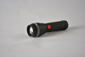 A black flashlight with a red button lies on a plain white surface.