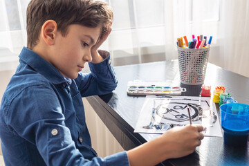 A sad young boy paints only in black, ignoring other colors, symbolizing childhood depression,...