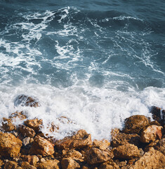 Deep blue water waves crashing on orange rocks