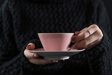 girl or woman with polished nails holding a pink cup of coffee with a saucer against a black background with negative space