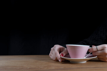girl or woman with polished nails holding a pink cup of coffee with a saucer against a black background with negative space