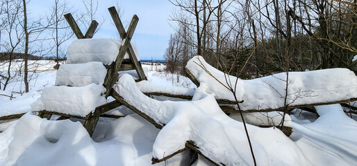 Deep snow layered on top of a wooden stile ladder over a wood rail fence.