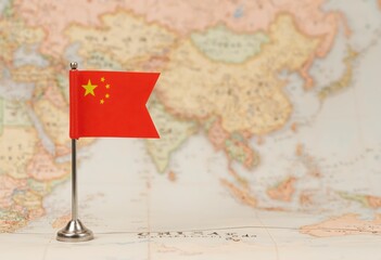 Naklejka premium Chinese flag on miniature pole placed on a vintage map background. Concept of geography, travel, and international relations. Close-up composition for design and print.