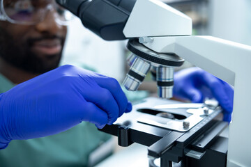 African American male scientist in lab using lens of microscope for study and research on health