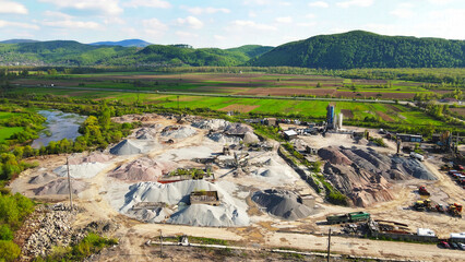 Aerial View of Quarry and Surrounding Fields. Aerial shot of a quarry with piles of gravel, construction equipment, and surrounding green fields and wooded hills in the background.