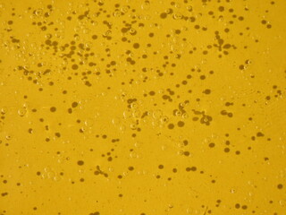 Shiny transparent bubbles of oil on water with yellow background.