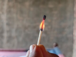 close-up of a burning matchstick with orange flame in a natural background