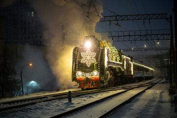Old retro Christmas steam train with brightly colored snowflake garland at night in the city on...